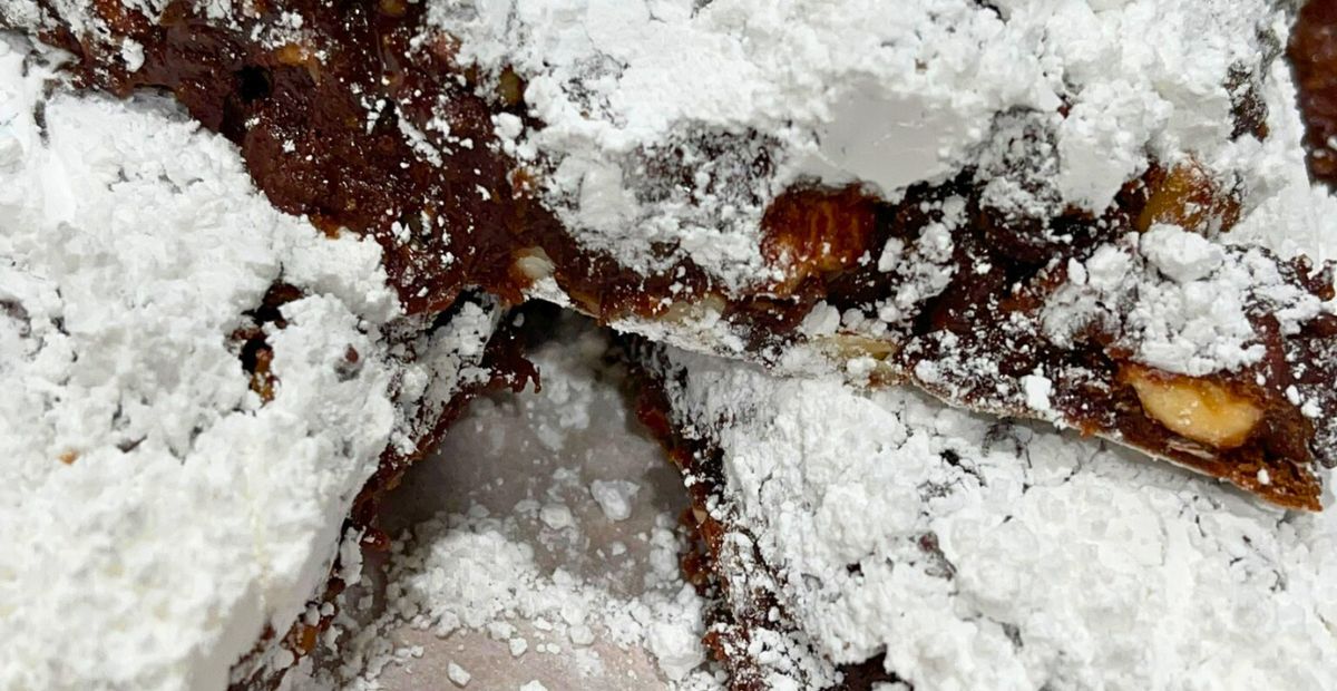 The confectioner's sugar being placed on then brushed of the Panforte 